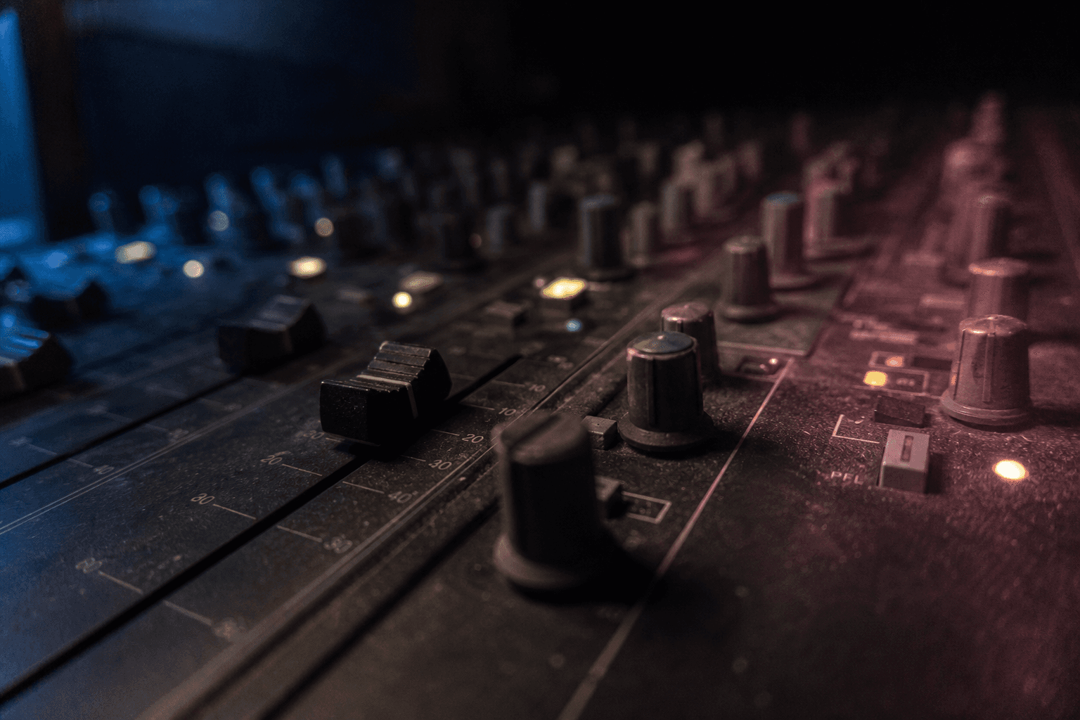 Close-up of mixing-desk faders and illuminated controls
